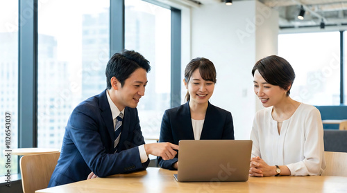 Three smiling business people looking at a laptop in a bright office teamwork and collaboration modern workplace