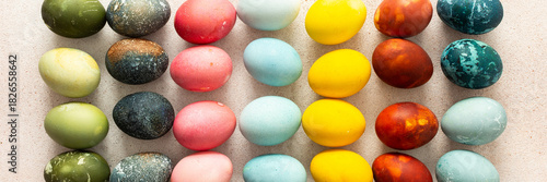 Dozens of beautifully colored Easter eggs in bright shades of green, pink, yellow, blue, and red are arranged in neat rows on a light background, ready for holiday festivities, banner