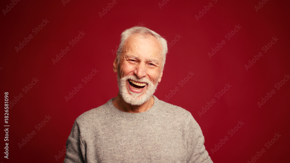 Obraz premium Portrait of smiling happy elderly man laughing looking at camera isolated on red background