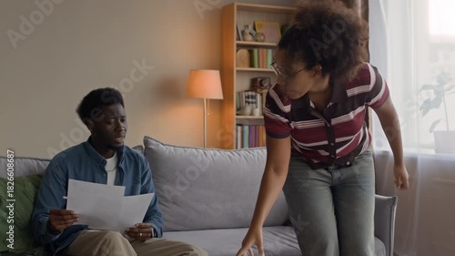 Medium shot of stressed couple arguing at home while looking over overdue bills and household expenses, showing frustration and worry about their financial situation