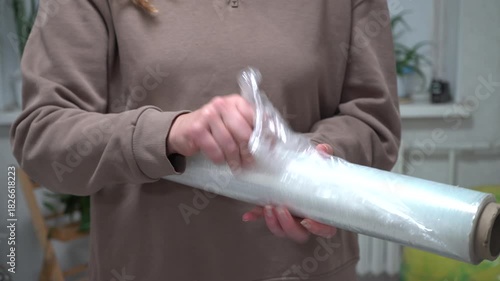A man unrolls plastic film from a roll in his hands