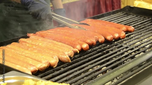 Close-up view of multiple sausages cooking on a hot grill at an outdoor food fair.
