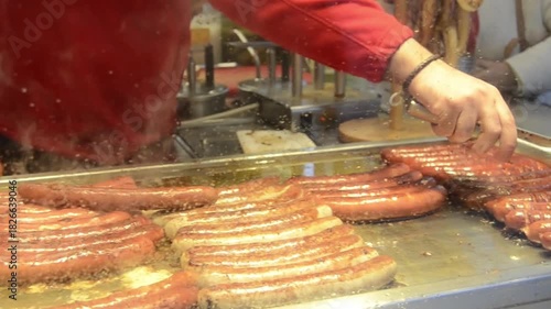 Close-up view of multiple sausages cooking on a hot grill at an outdoor food fair.