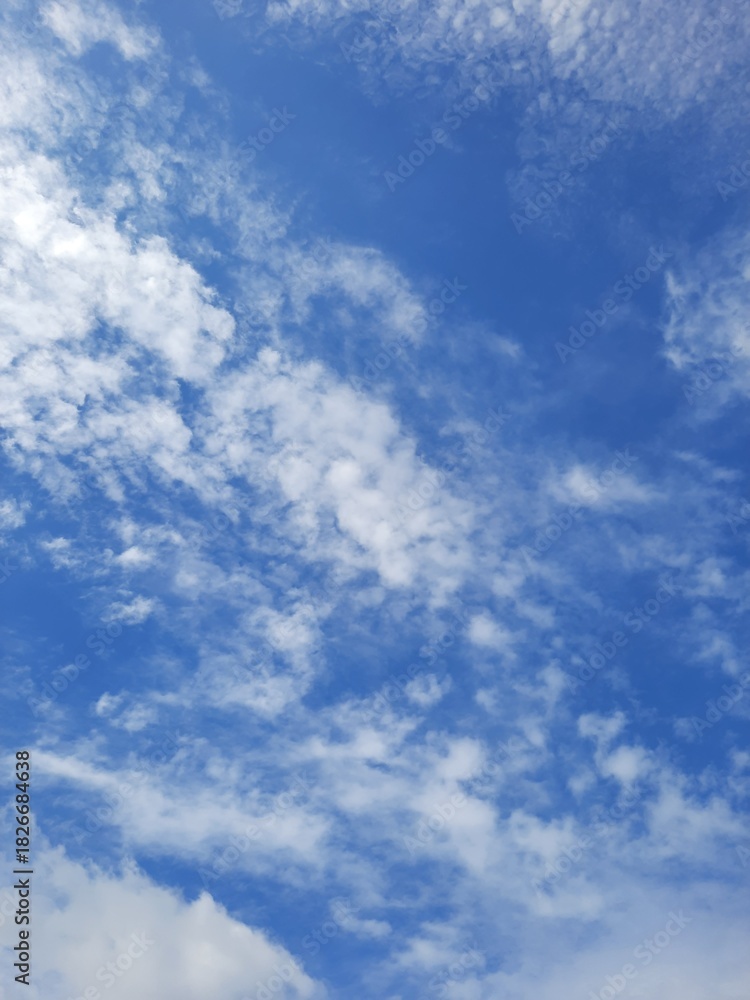 Fototapeta premium Scattered white clouds floating in a bright blue sky on a clear day