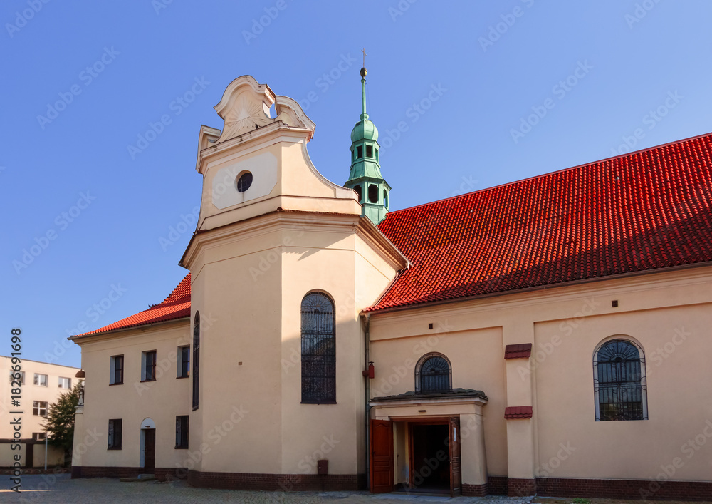 Naklejka premium Panoramic Front Facade of Red Brick Church with Yellow Walls. Roman Catholic Church at Wawrzyńca Street in Gniezno, Greater Poland Voivodeship, Poland