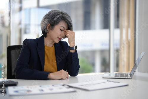 Older Asian businesswoman confronts work stress fatigue office burnout senior professional navigating modern corporate pressure