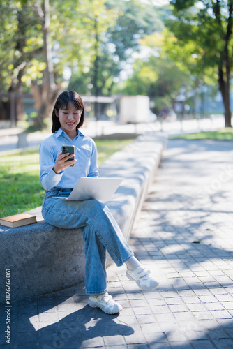Young student using laptop and smartphone outdoors in park