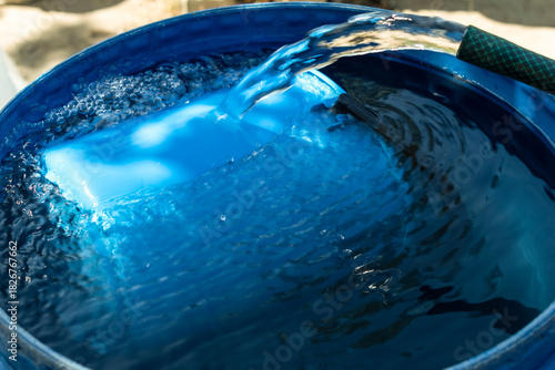 A clear stream of water flows into a blue barrel with a floating bucket.