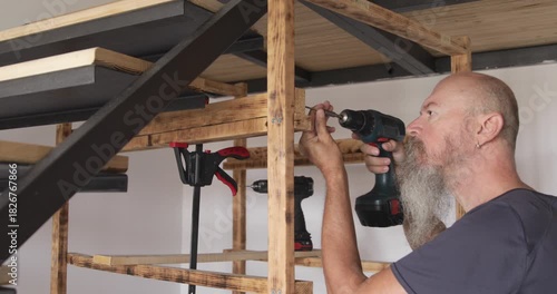 50 year craftsman assembling wooden shelf at home, securing slates using electric screwdriver, real people