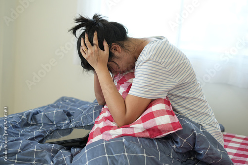 Young asian woman is feeling sad, tired, stressed and worried suffering depression in mental health, and she is lying on bed, using tablet and covering her ears and cannot sleep well from insomnia.