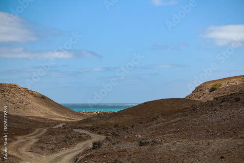 Gravel road through arid hills winding to the blue ocean (Boa Vista Island, Cabo Verde, Africa)