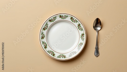 Overhead view of a festive holiday plate with holly border and antique silver spoon on beige surface