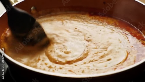 A creamy sauce is being stirred in a pan. The sauce is a mix of white and orange-red hues