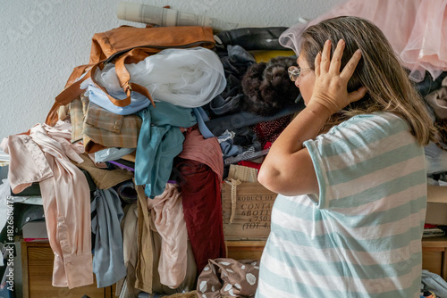 Photos woman standing huge pile mixed clothes, fabrics stacked chaotically, overwhelmed