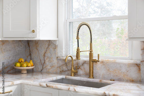 A gold kitchen faucet detail with white cabinets, stainless steel sink, and granite countertops.