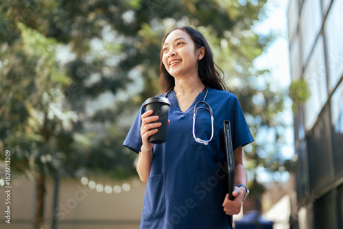 Asian nurse enjoying coffee break walking outdoors