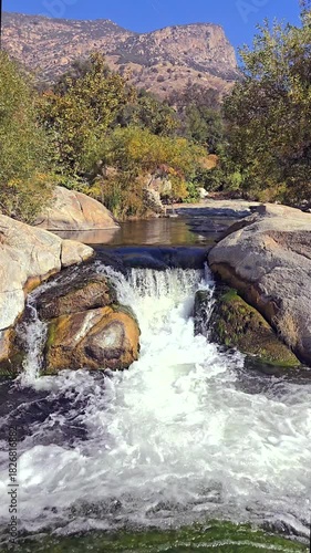A serene waterfall flowing over rocks in a lush, mountainous landscape.