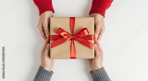 Top view of two people exchanging a beautifully wrapped brown paper gift box with a bright red ribbon and bow isolated on white background