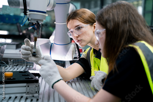 Two women wearing safety goggles and gloves are working on a machine