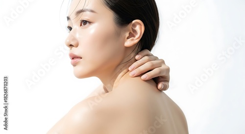 Closeup portrait of a young woman with clear, glowing skin touching her neck against a bright white background