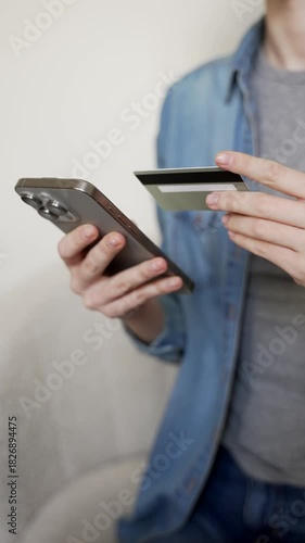 Vertical view of a woman's holding a credit card and using a smartphone for online shopping, entering payment details for a secure transaction on the internet, mobile banking. Close up.