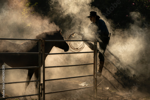 A cowboy training a horse in a dusty corral at sunrise, creating a dramatic western silhouette
