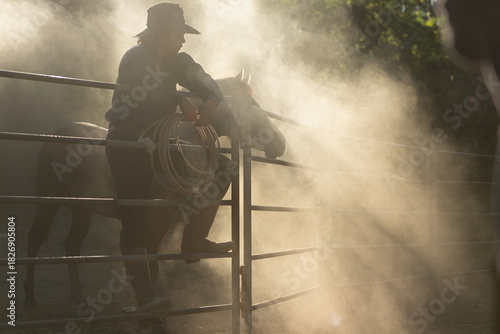A cowboy training a horse in a dusty corral at sunrise, creating a dramatic western silhouette