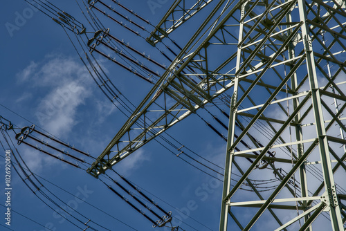 A German electricity pylon stands against a clear blue sky, showing the power transmission network. The steel mast supports the electric grid and the energy transition.