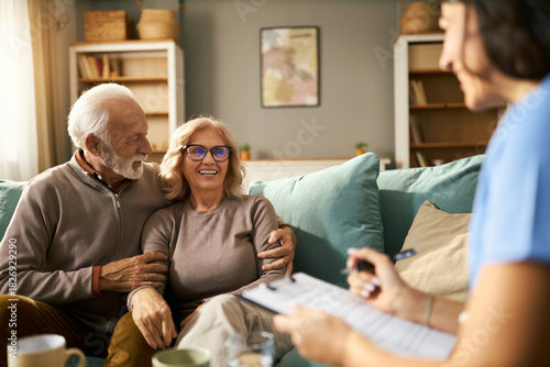 Happy senior couple talking to female doctor during her home visit
