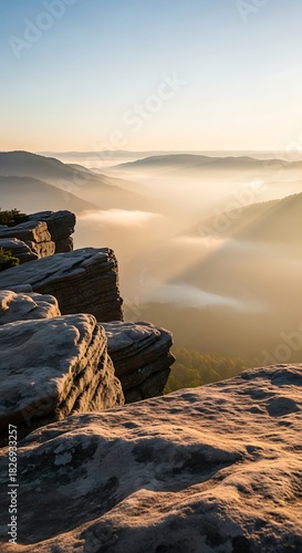 Sunrise over a misty mountain valley, with rugged rock formations in the foreground and golden light illuminating the landscape
