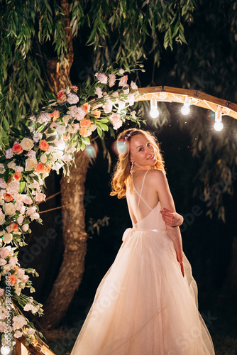 blonde bride in a light coral dress against the backdrop of an evening round arch
