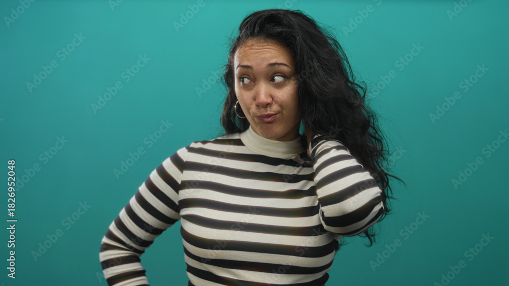 Fototapeta premium Woman touching and inspecting long dark hair in a teal studio wearing a striped turtleneck; contemplation.