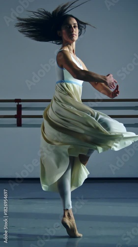Slow motion vertical shot of graceful contemporary female dancer practices with focus and elegance in dance school or gym, refining her technique and expression through rigorous training, dedication.