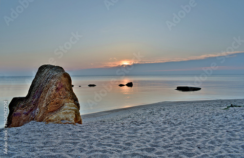 Calm sea and sandy beach early in the morning. Some large stones on the shore and in the water.