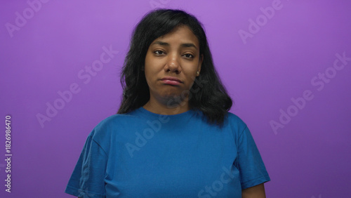 Woman face frowning slightly looking at camera under soft lighting in purple studio; boredom fatigue.