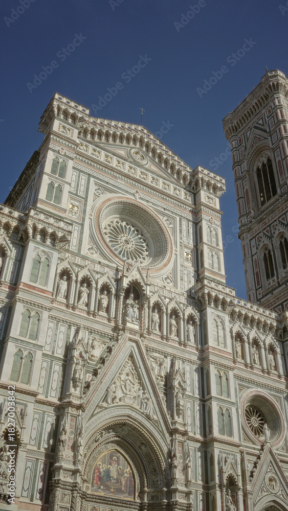 Obraz premium Campanile and cathedral facade standing tall with detailed green white and pink marble ornament, rose window and statues on a building in florence italy; awe.