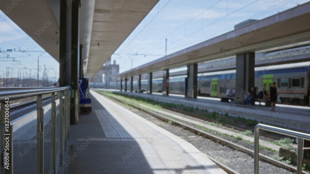 Naklejka premium Train station scene on a platform in shallow blurred focus with soft bokeh and distant trains and tracks visible; background backplate copyspace calm.