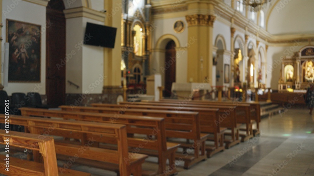 Fototapeta premium Defocused interior church scene with soft blurred wooden pews and distant altar, shallow bokeh; backdrop copyspace backplate calm.