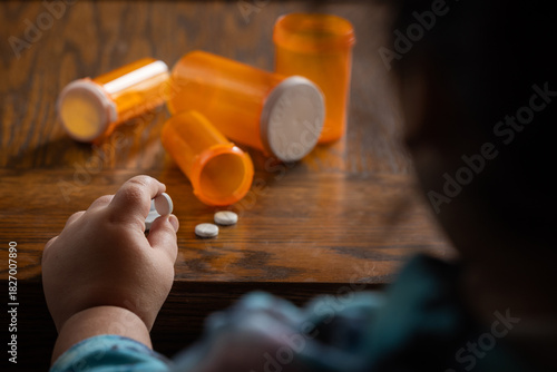 A powerful conceptual photograph showing a child's hand reaching for colorful, unattended prescription pills or medication.