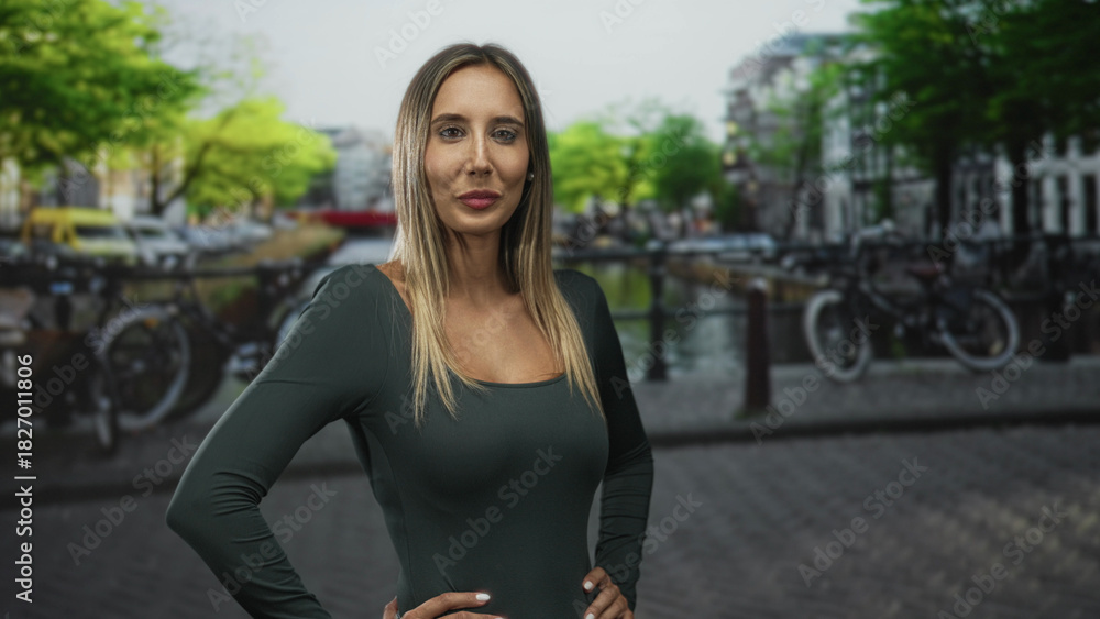 Fototapeta premium Woman with hands on hips showing shoulders at street canal in amsterdam; confidence travel exploration.