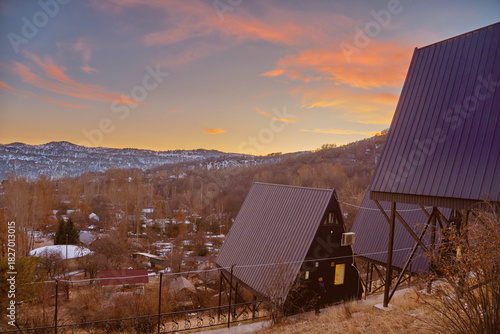 A-frame cabins on snowy hillside at sunrise, under construction, forest retreat with mountain view.