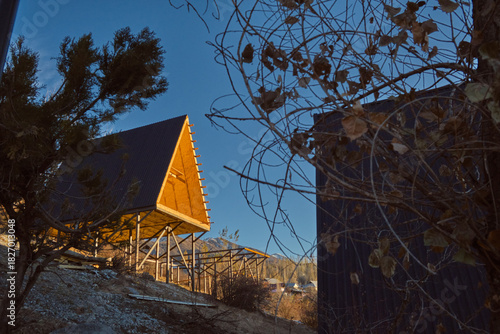 A-frame cabins on stilts in forest at sunset, minimalist autumn retreat with metal roofs and wood interiors.