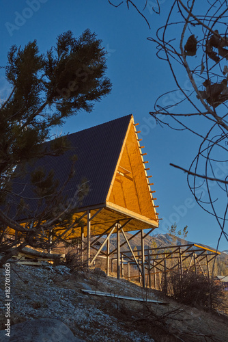A-frame cabins on stilts in forest at sunset, minimalist autumn retreat with metal roofs and wood interiors.