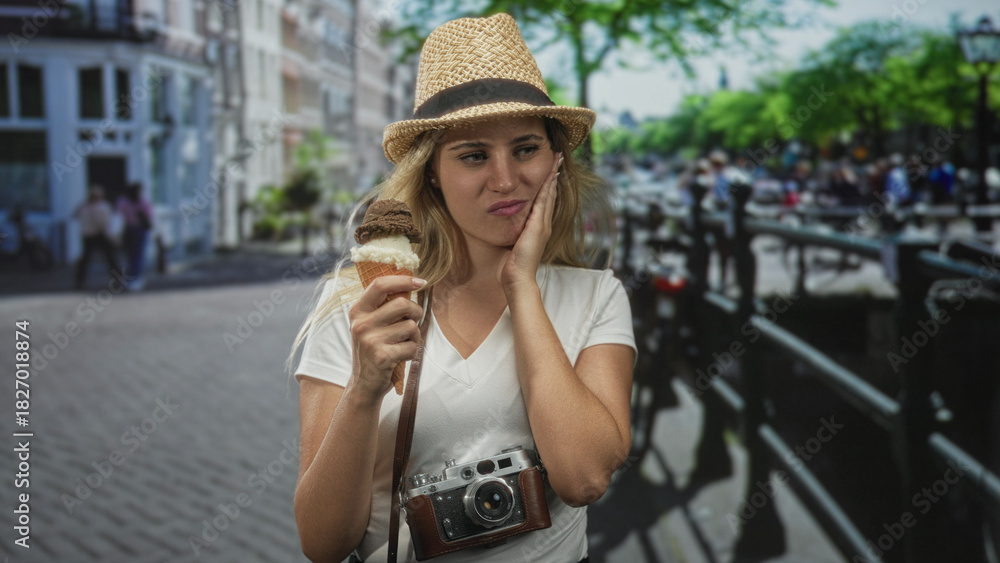 Fototapeta premium Woman holding ice cream cone with hand on cheek for toothache and vintage camera around neck on a city street; discomfort.