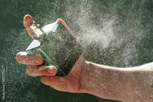 A hand holds a bottle of perfume spraying the liquid into a fine diffusion in the beautiful sunset light