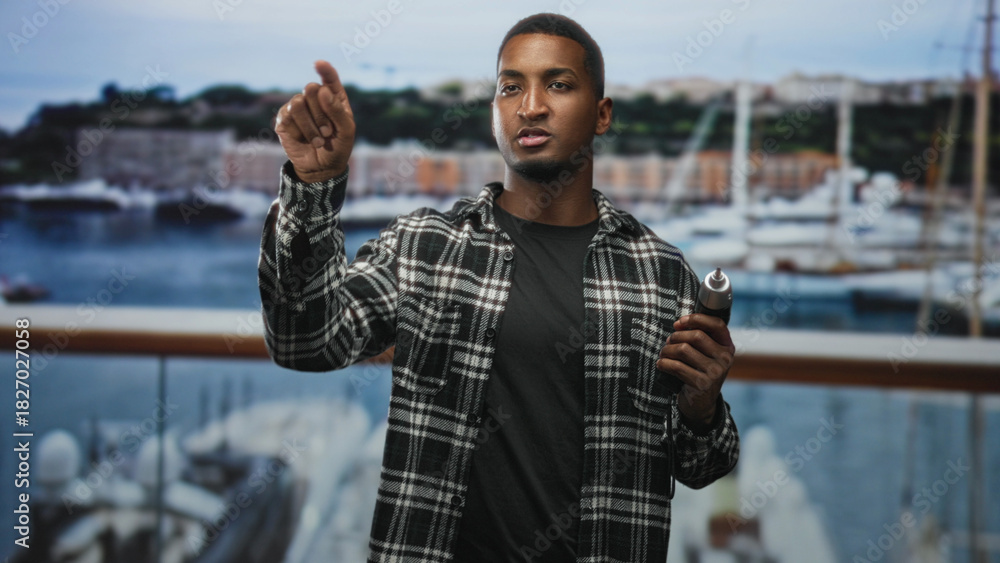 Fototapeta premium Man holding electric screwdriver points finger toward camera on balcony of building, right hand gripping tool and thumb visible; skill confidence.
