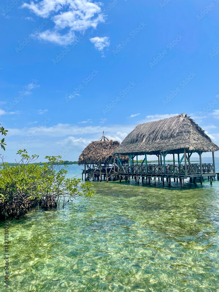 Fototapeta premium Thatched hut on wooden stilts over clear Caribbean waters near Bocas del Toro, Panama. Cloudy tropical sky