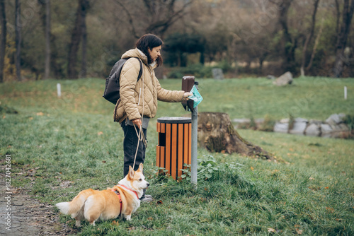 Person with a dog uses a waste disposal station in a park on a cloudy day