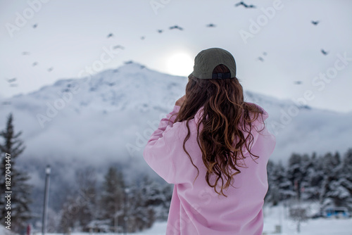Person Photographing Snowy Mountain Landscape with a Smartphone as Birds Fly Over a Winter Peak Under Soft Morning Light