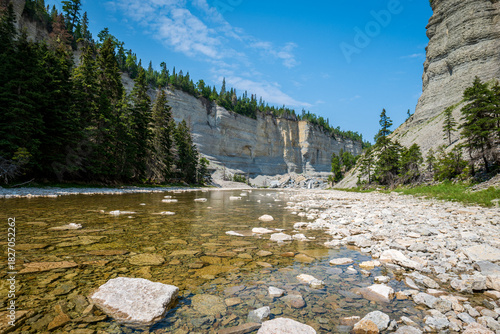 Steep Canyon, Stone Cliffs, Shallow River, Fallen Boulders, and Boreal Forest Under a Blue Sky near to Vaureal Waterfall on a Sunny Day in Anticosti, Quebec, Canda